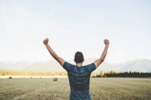 A man in a blue t-shirt stands in a field with his arms raised above his head in celebration of his reliable move in Ottawa.