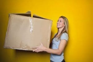 Woman in grey shirt holding brown cardboard moving box.