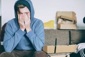 Young man holds his head in his hands with packing boxes in the background